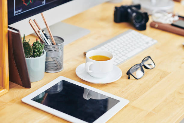 Digital camera with empty screen, cup of coffee, glasses and pot with glasses on office desk of entrepreneur