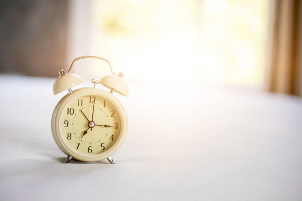 istock Analog alarm clock on white bed, time in the morning with a bright sunshine 1168881815