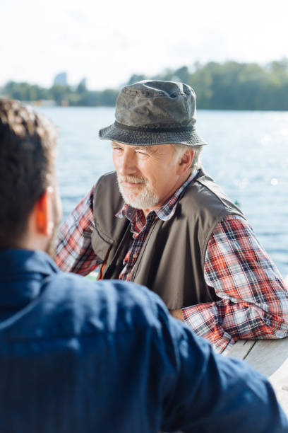 istock Bearded retired man speaking with son while sitting near lake 1168883630
