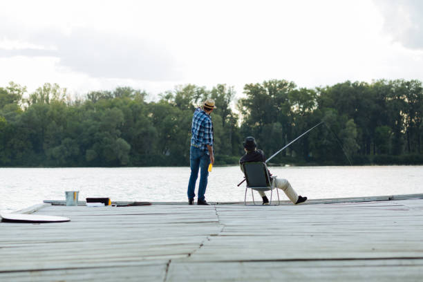 istock Man wearing hat talking to father sitting and catching fish 1168883733