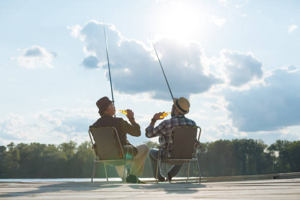 istock Father and son sitting in chairs and drinking beer while fishing 1168883734