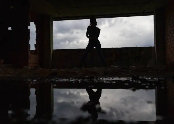Silhouette of woman caucasian hip hop dancer, freestyling outdoors in an old abandoned building with refelection in puddle