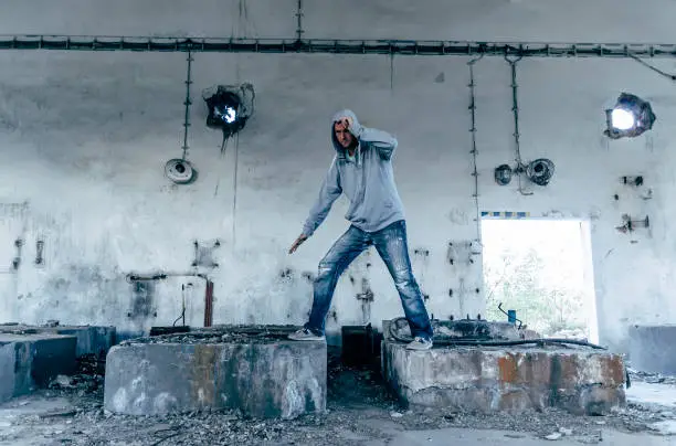 Portrait of a handsome caucasian hip hop dancer, freestyling outdoors in an old abandoned building, blue toned