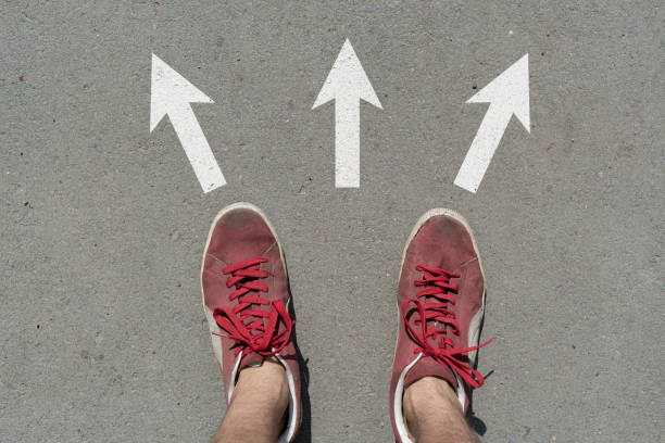 istock difficult to choose where to go, feet stand on the asphalt abstract surface with arrows 1168889269
