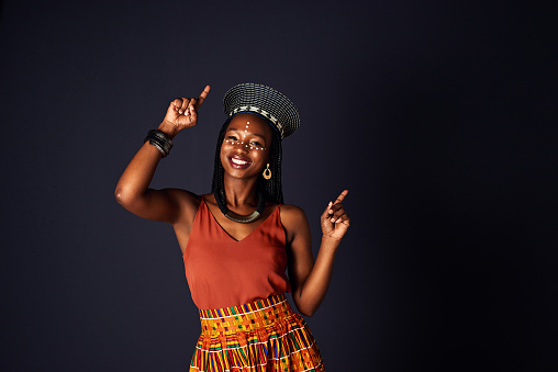Studio shot of an attractive young woman dressed in traditional african attire dancing against a black background
