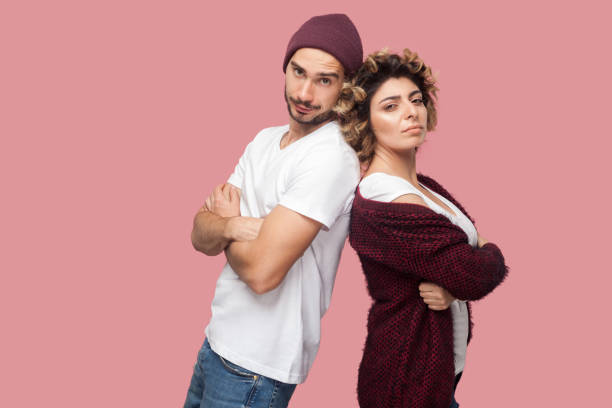 Portrait of serious couple of friends in casual style standing back to back, crossing arms and looking at camera with proud face. Portrait of serious couple of friends in casual style standing back to back, crossing arms and looking at camera with proud face. Isolated, indoor, studio shot, pink background celebrity endorsements stock pictures, royalty-free photos & images