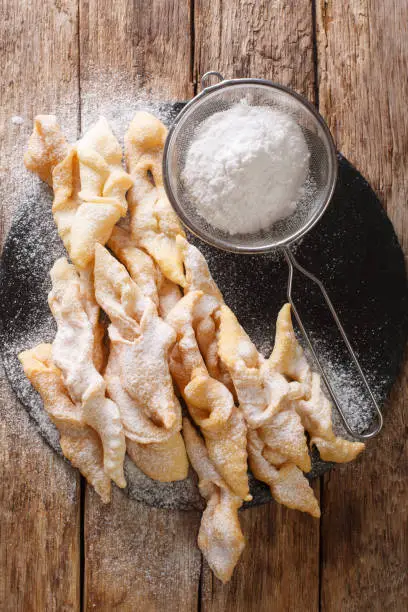 Freshly made Angel Wings Cookies with powdered sugar close-up on the table. Vertical top view from above