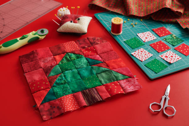 blocco patchwork albero di natale, tappetino artigianale, pezzi quadrati luminosi di tessuto, pincushion come babbo natale e accessori trapuntatura su sfondo rosso - quilt patchwork sewing textile foto e immagini stock