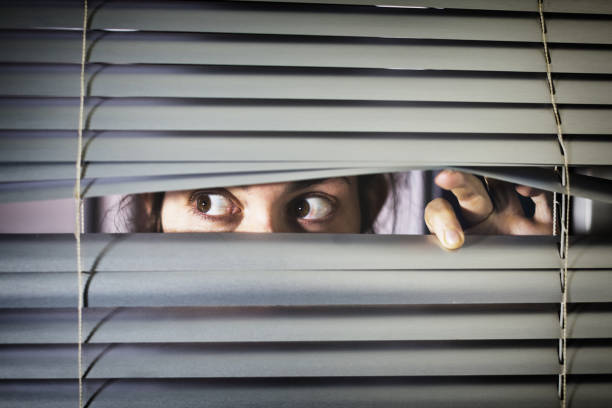 Brown-eyed girl peeps fearfully through venetian blinds A young woman with brown eyes looks sideways nervous through closed blinds. woman stealth stock pictures, royalty-free photos & images