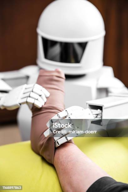 Caregiver Robot Or Medical Assisted Living Robot Is Putting On A Compression Stocking On An Senior Adults Leg Stock Photo - Download Image Now