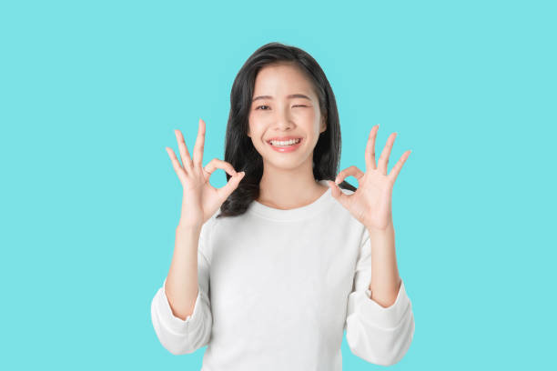 porträt glücklich asiatische frau zeigt ok zeichen und lächelnde hexe blick auf die kamera auf blauem hintergrund, fröhliche mädchen gesten studio. - child lifestyles isolated blue stock-fotos und bilder