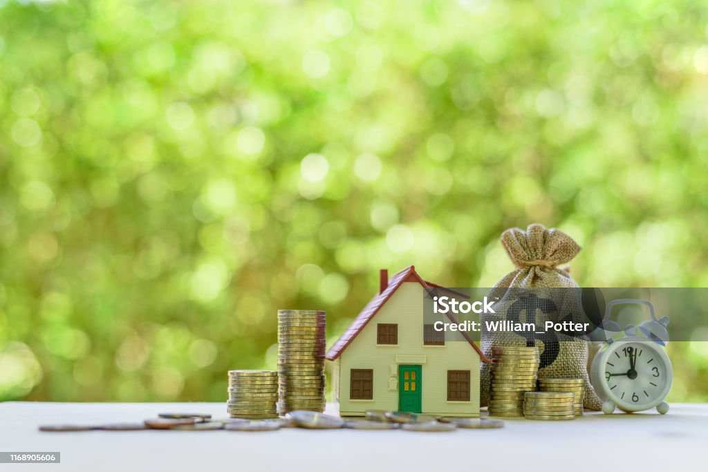 Residential real estate loan, financial concept : House model, coins, US dollar bag, white clock on a table, depicts home loan or borrowing money to buy / purchase a new home for first time homebuyer Real Estate Stock Photo