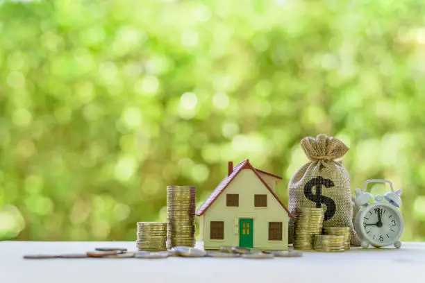 Photo of Residential real estate loan, financial concept : House model, coins, US dollar bag, white clock on a table, depicts home loan or borrowing money to buy / purchase a new home for first time homebuyer