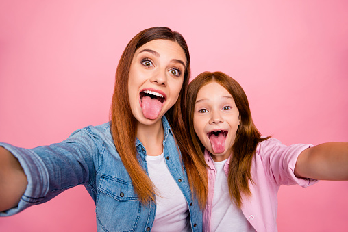 Close up photo of sweet people, with attractive long hairstyle making faces wearing denim jeans shirts isolated over pink background