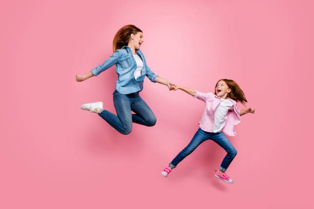 キツネの小さな女性と彼女の興奮したママジャンプ高い歩くおもちゃの店の写真は、カジュアルなジーンズの衣装孤立したピンクの背景を着用 - isolated little girls two people child ストックフォトと画像