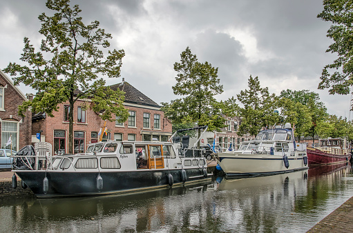 Meppel, The Netherlands, August 1, 2019: Yachts moored at Heerengracht canal with low bricks houses in the background, under a cloudy sky,