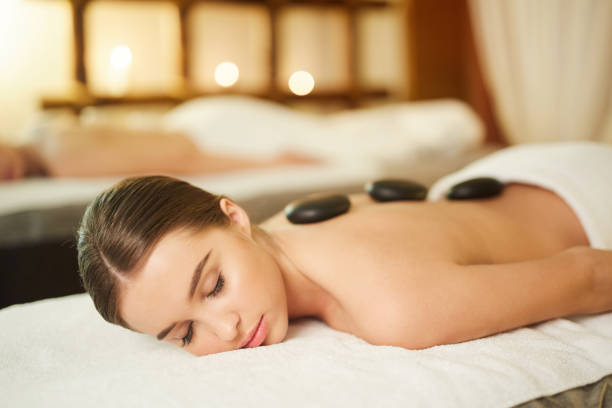 belle femme enjoyinf thérapie de pierre dans la spa de luxe - lastone therapy massaging spa treatment stone photos et images de collection