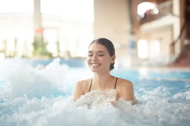 Portrait of beautiful young woman smiling happily while enjoying bubbly hot tub in SPA, copy space