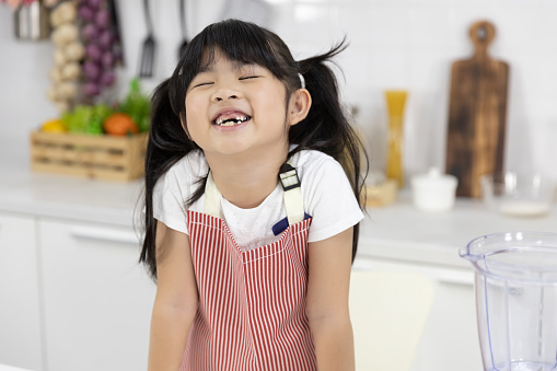 Portrait of Happy Asian Little girl smiling in Apron set cooking food in kitchen at home.