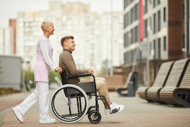 istock Content attractive qualified nurse in uniform strolling with disabled patient in city, she pushing wheelchair with man 1168910234