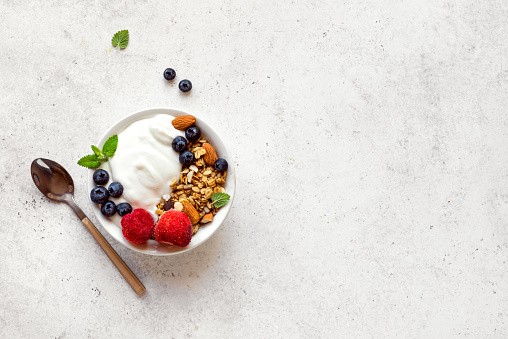 Granola with yogurt and berries for healthy breakfast. Bowl of greek yogurt with granola, almonds, blueberries and strawberries, top view, copy space.