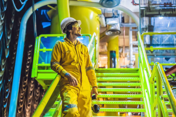joven con un uniforme de trabajo amarillo, gafas y casco en el entorno industrial, plataforma de petróleo o planta de gas licuado - oil rig oil construction sea fotografías e imágenes de stock