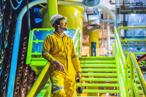 giovane in uniforme da lavoro gialla, occhiali e casco in ambiente industriale, piattaforma petrolifera o impianto di gas liquefatto - working platform foto e immagini stock