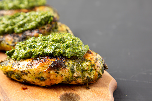Grilled chimichurri chicken breast on a rustic wooden board on a black background, side view. Close-up. Copy space.