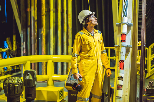Young man in a yellow work uniform, glasses and helmet in industrial environment,oil Platform or liquefied gas plant.