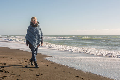 Mature woman with poncho that walks on the seashore in autumn