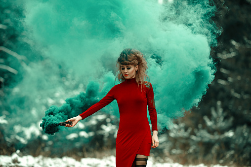 Woman wearing red dress holding flaming torch in the forest