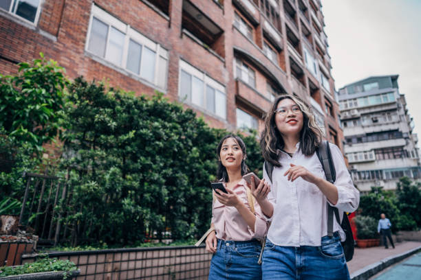 deux étudiants de filles sur la rue utilisant des téléphones - smart casual outdoors friendship happiness photos et images de collection