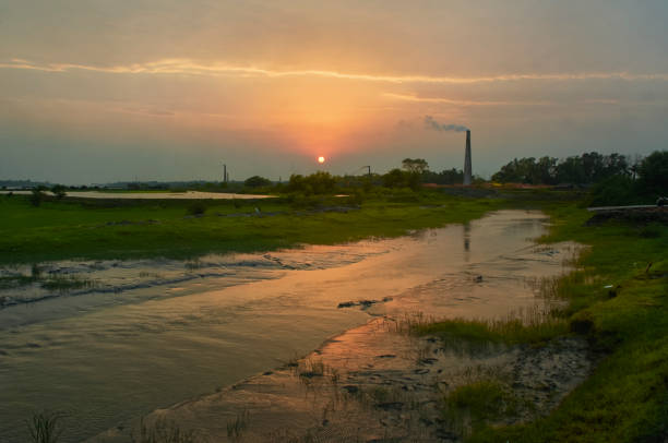 Ichamati riverbank during sunset at Taki, in West Bengal. Smoke coming from chimneys of brick manufacturing factories are visible in background. Large number of brick factories are present near riverbanks.