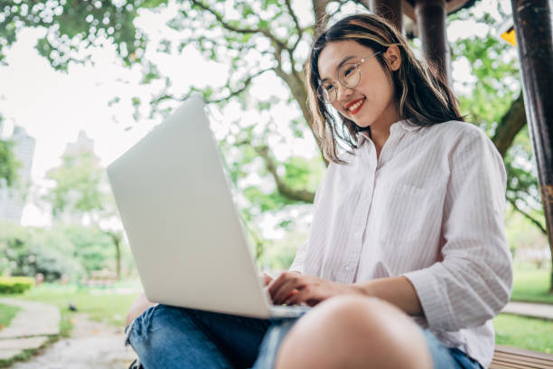 Woman student using laptop in park One woman, young woman student sitting alone in park, using laptop. asian adult student stock pictures, royalty-free photos & images