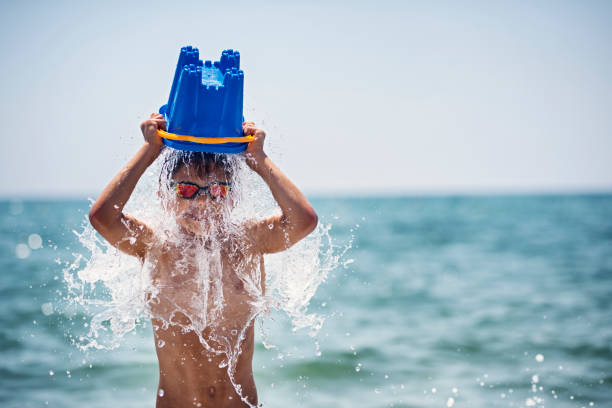 niño enfriándose con cubo de agua - spraying beaches summer sunlight fotografías e imágenes de stock