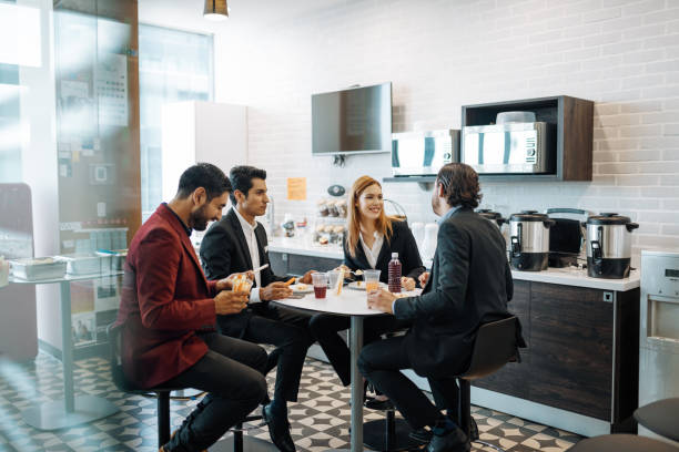 millennial latin mitarbeiter, die eine pause bei der arbeit machen, snacks essen und plaudern. - kantine stock-fotos und bilder