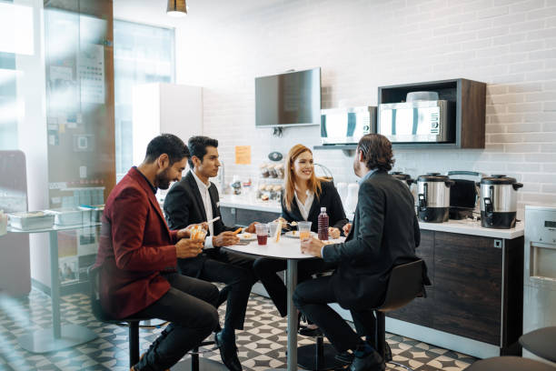 Millennial Latin coworkers taking a break at work, eating snack and chatting. stock photo