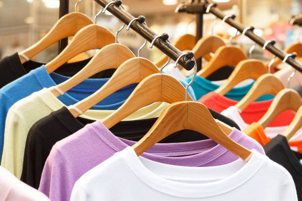 Multicolored t-shirts on wooden hangers in store, front view. stock photo