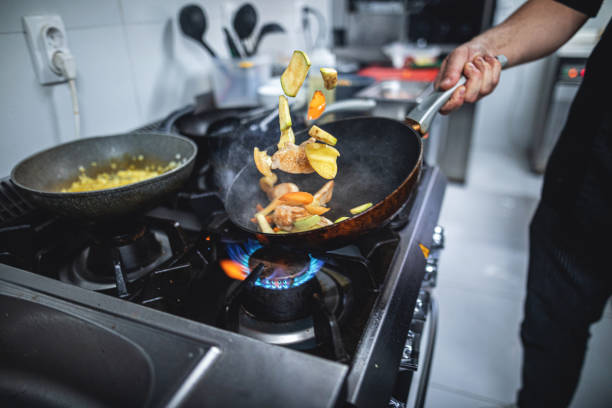 Chef preparing food over a flaming gas stove Skilled chef preparing gourmet food at a restaurant kitchen. gas stove burner stock pictures, royalty-free photos & images