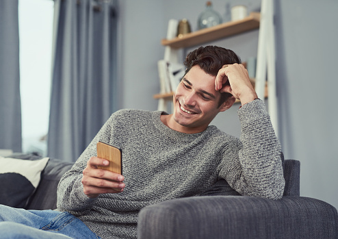 Shot of a young man using a cellphone while relaxing at home