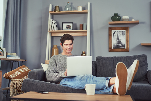 Shot of a young man using a laptop while relaxing at home