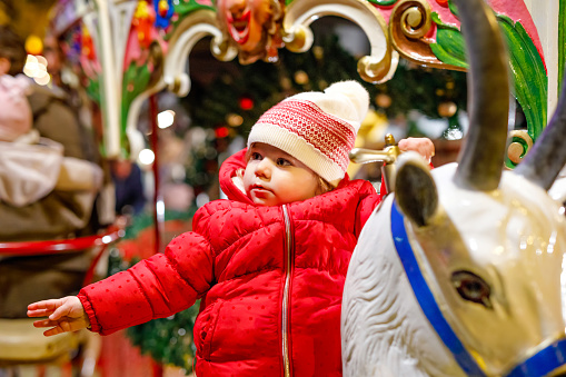 Adorable little kid girl riding on a merry go round carousel horse at Christmas funfair or market, outdoors. Happy toddler child having fun on traditional family xmas market in Germany