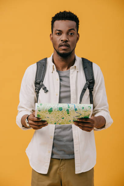 handsome african american man with backpack holding map isolated on orange