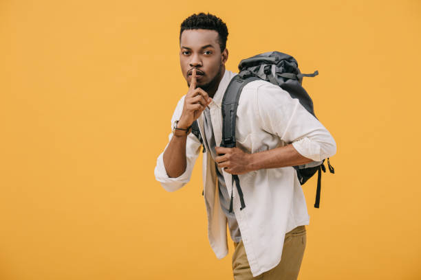 istock african american man showing hush sign while standing with backpack isolated on orange 1168956905
