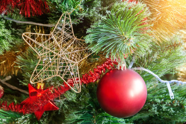 istock Green artificial Christmas tree decorated with star in a golden frame and interlacing golden threads; red matte ball; and yellow and red garlands. Home decoration for a family holiday. Selective focus 1168966123