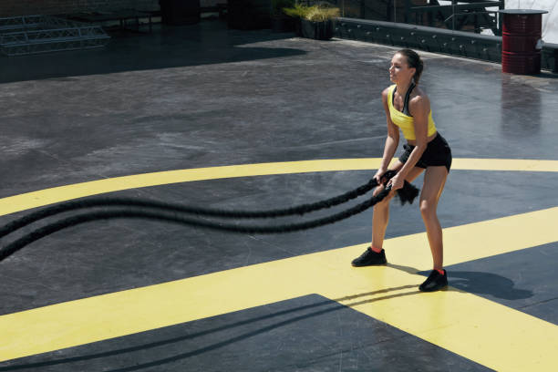 Sport woman doing battle ropes exercise workout at gym