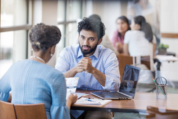 Serious bank officer talking with customer As a female customer reviews a bank brochure, a male bank employee explains the loan application process. credit union stock pictures, royalty-free photos & images