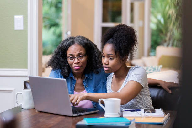 Young woman shows her mom something on laptop Young woman and her mature mom look at something on a laptop as the young woman studies for a college exam. college student and parent stock pictures, royalty-free photos & images