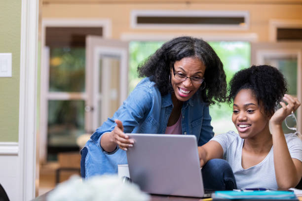 Cheerful mom and daughter use laptop Smiling mature woman and her daughter look at something on a laptop as the daughter studies for a test. college student and parent stock pictures, royalty-free photos & images