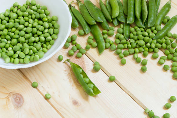 istock Sugar snap peas background with copy space. Peeled beans scattered on wooden table and collected in a white bowl, lot of whole pods. 1168974636